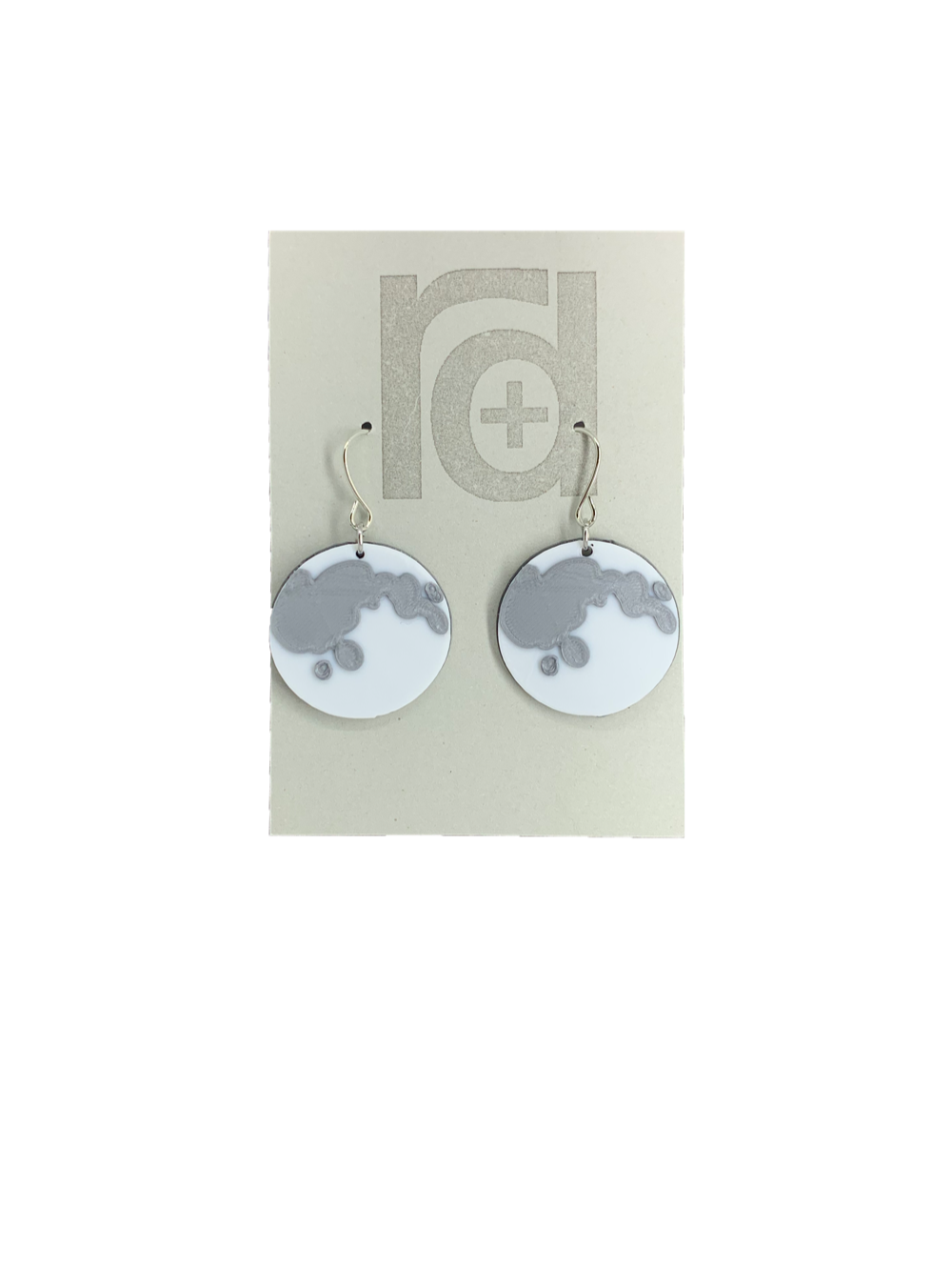 On a grey R+D earring card there are 2 3D printed hook earrings. They pendant on the hook is about an inch wide and a perfect full moon. It is bright white with silver accents to look like the natural creators on the face of the moon. The reverse of the moon in black. 
