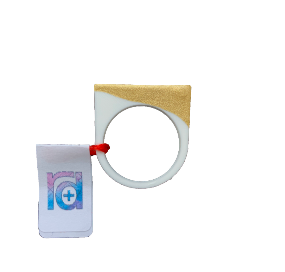 Show straight on with a R+D tag is a 3D printed ring. It is printed in a white plant based filament and dipped in a gold paint. The ring is a smooth circle around the finger, but extends into a square shape at the top.