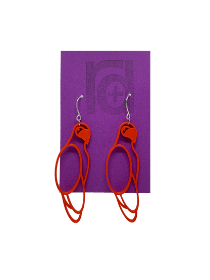 Hanging from a bright purple earring card are two R+D 3D printed earrings. The earrings are red outlines of parrots.