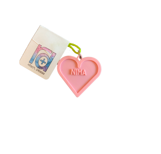 A light pink 3D printed pet tag is in the middle of the photo. It is the shape of a heart with the name NIMA in the middle. This can be customized to 16 other colors and with any name. 