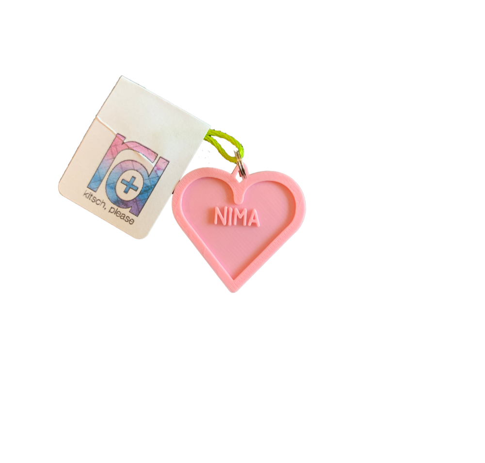 A light pink 3D printed pet tag is in the middle of the photo. It is the shape of a heart with the name NIMA in the middle. This can be customized to 16 other colors and with any name. 