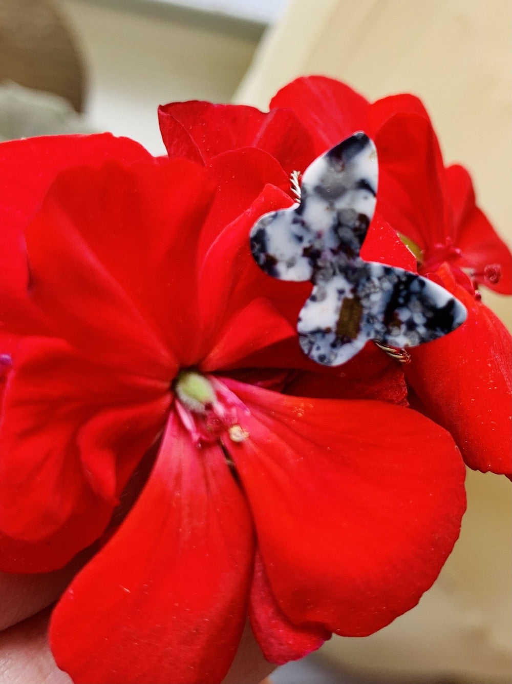On a bright red geranium is a butterfly shaped ring. It is cast from recycled 3D prints in black, white and silver plant based filaments. They have a speckled look like granite.