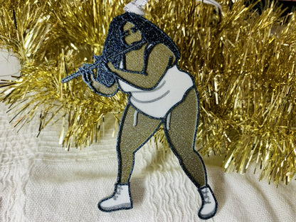 On a white fabric background there is an R+D 3D printed ornament resting on a pile of gold garland. The ornament is shaped like Lizzo while she plays her flute. She is gold, silver, white, and black and the entire ornament has been covered in glitter to shimmer in the light.
