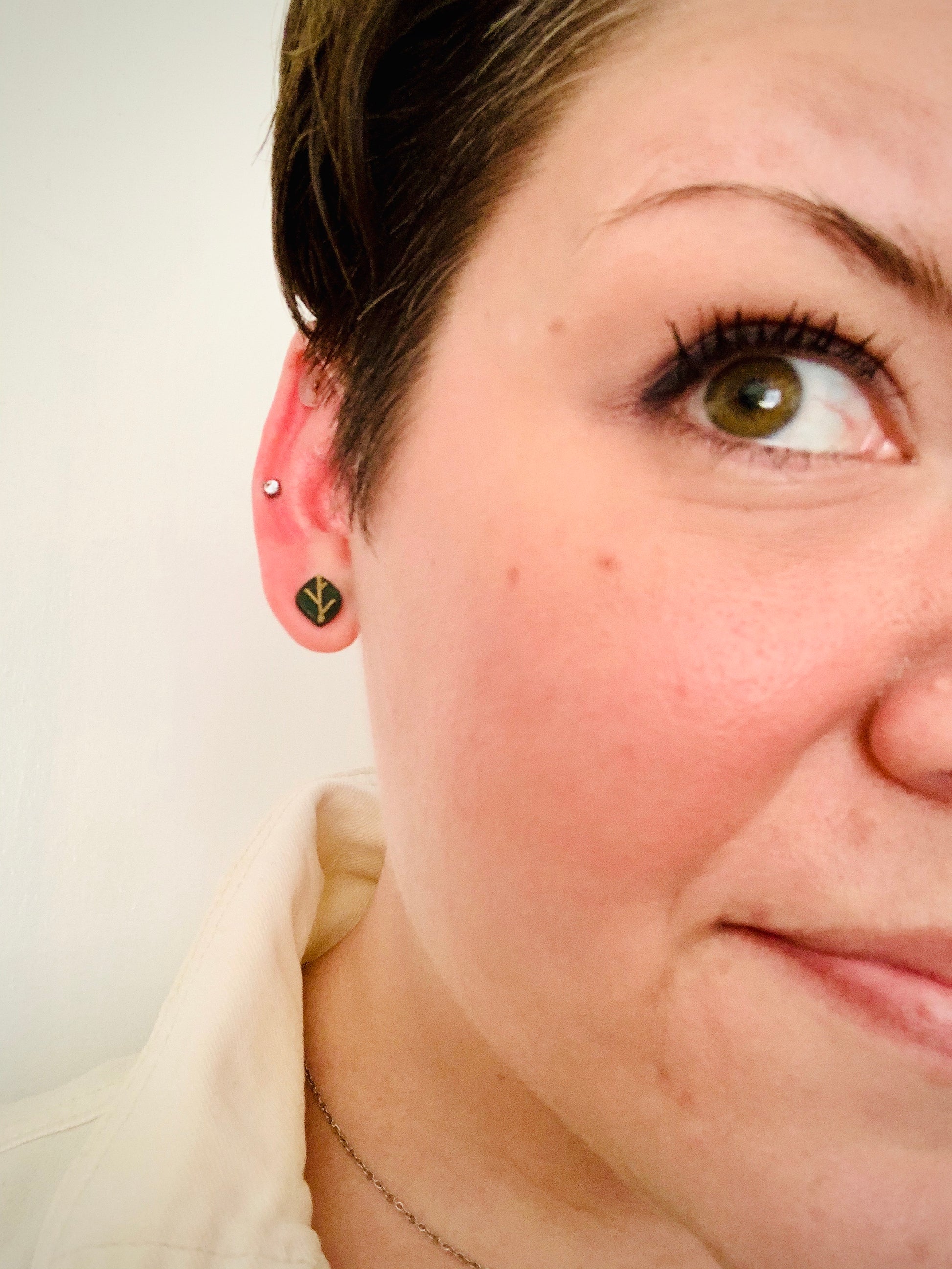 A close up of R+D owner Rebekah Thornhill. IYou can see on her earlobe a R+D earring shaped like a leaf. The 3D printed  leaf is olive green with gold veins.