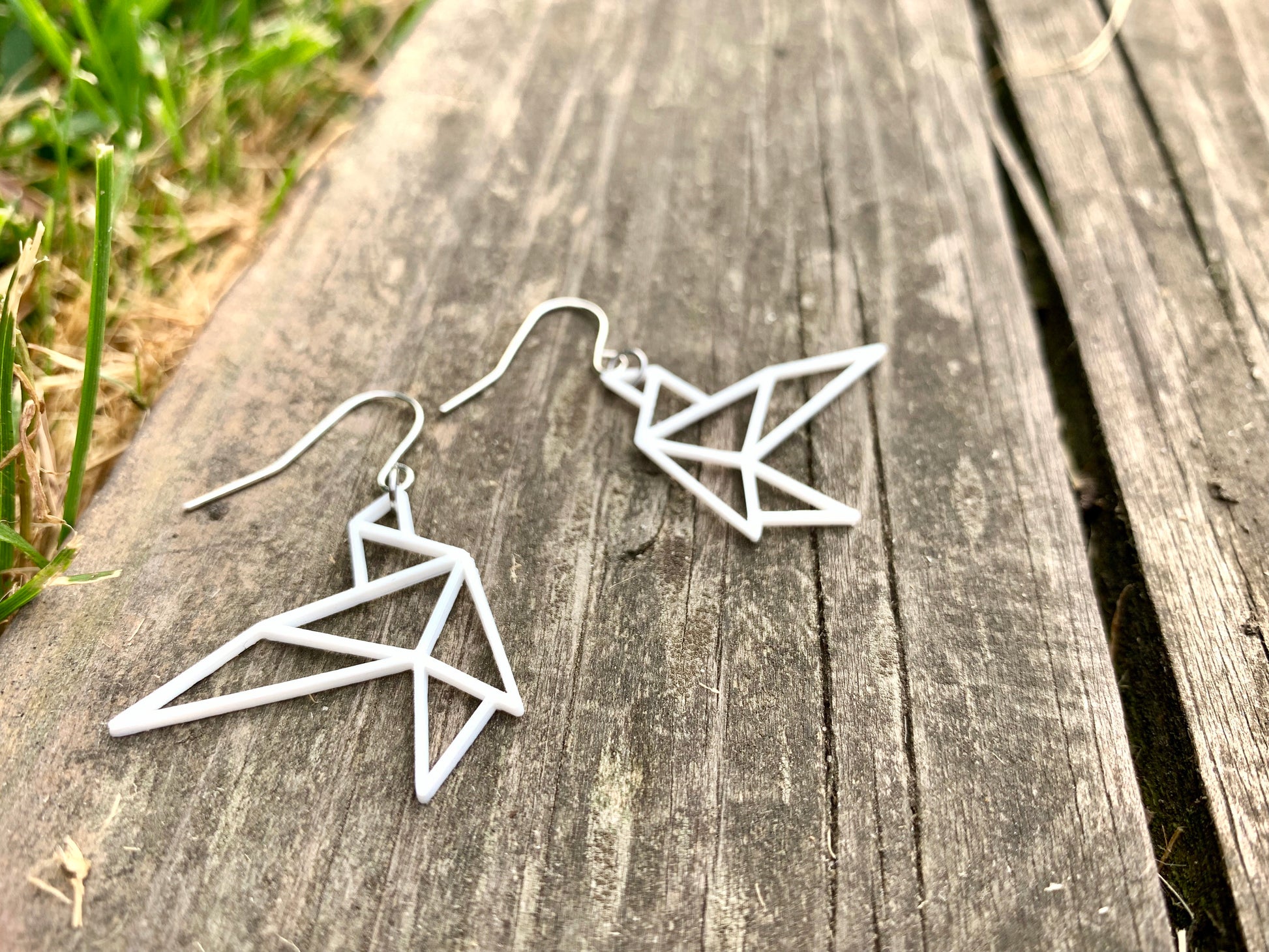 Laying on a old weathered piece of wood are two R+D earrings. They are shaped as geometric birds in flight. They are printed in a sustainable white filament that is plant based.