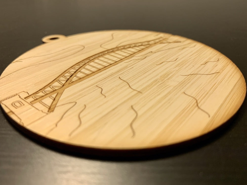 Shown from the side so you can see the detail is a laser cut wall hanging. It is cut from bamboo, a fast growing and sustainable grass. Etched in it a picture of the Hell Gate bridge in Astoria. This bridge is an icon of the area and looked on from Asttoria Park. This can be used as a ornament in the holidays or a wall hanging all year round. It can be painted like a paint by number or left plain.