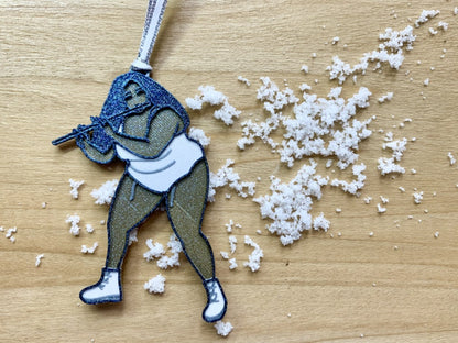 On a light wood shelf is a scattering of snow. Resting on top of this is a R+D 3D printed ornament. The ornament is shaped like the singer, rapper, and musician Lizzo. She is wearing a white leotard, bend slightly, and playing her flute name Sasha Flute. The entire ornament is printed with a plant based filament and covered in glitter to give it a perfect shimmer and shine.
