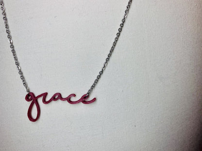 Hanging to the left on a white background  is a 3D printed pendant. In a modern cursive script it says grace in a dark red merlot color. 