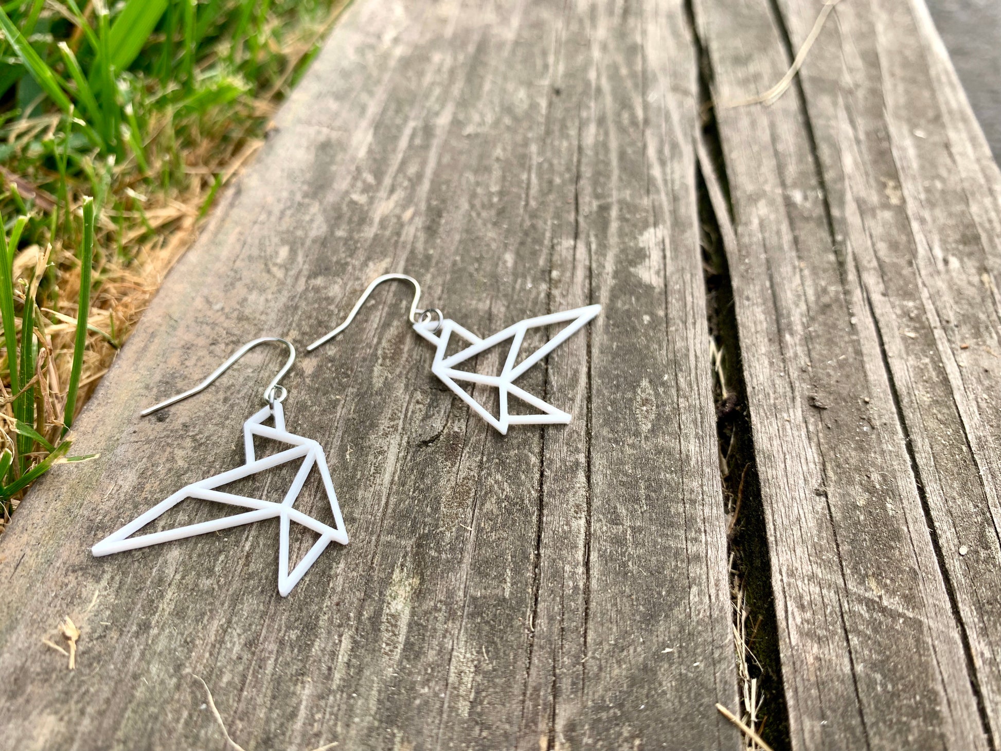 Laying on a old weathered piece of wood are two R+D earrings. They are shaped as geometric birds in flight. They are printed in a sustainable white filament that is plant based.