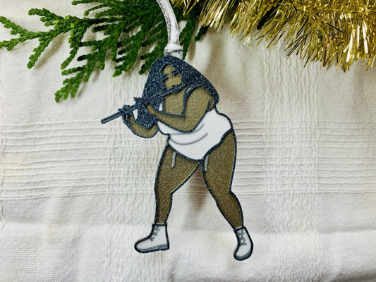 On a white fabric background you can see a 3D printed ornament hanging from a Christmas tree branch and gold garland. The ornament is shaped like Lizzo while she plays her flute. She is gold, silver, white, and black and the entire ornament has been covered in glitter to shimmer in the light.