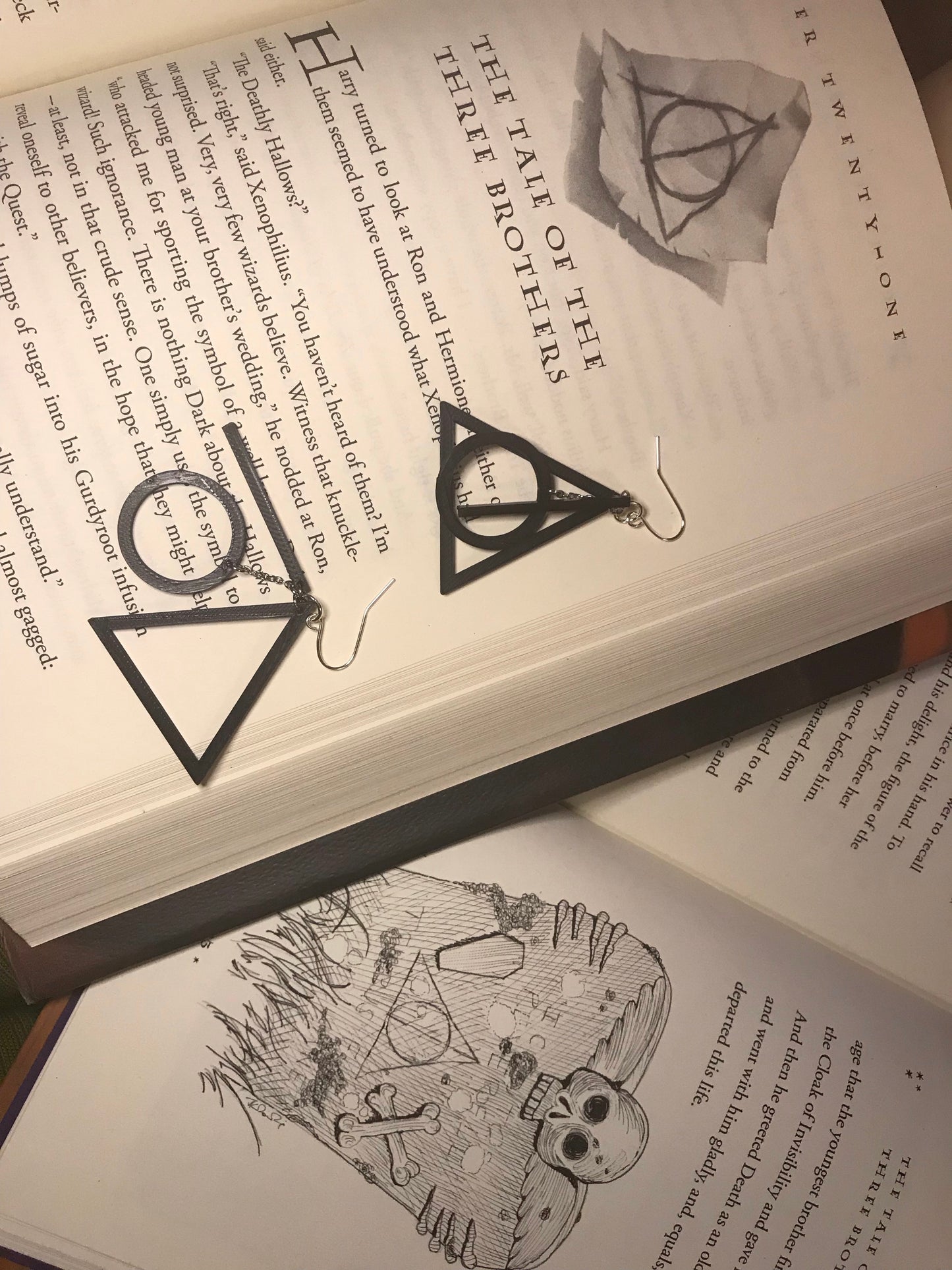 Shown on open books are two R+D earrings. One is stacked to see the symbol the three pieces form. The other is speed out to see the black line, black circle, and black triangle.