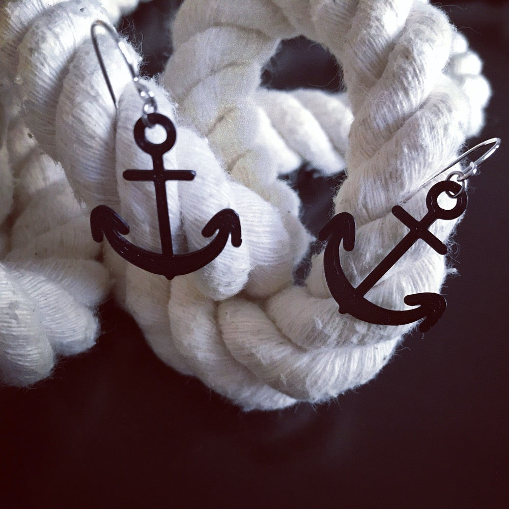 Two black earrings are shown on a thick cotton rope. The earrings are shaped like anchors and 3D printed using a environmentally friendly material made from corn. 