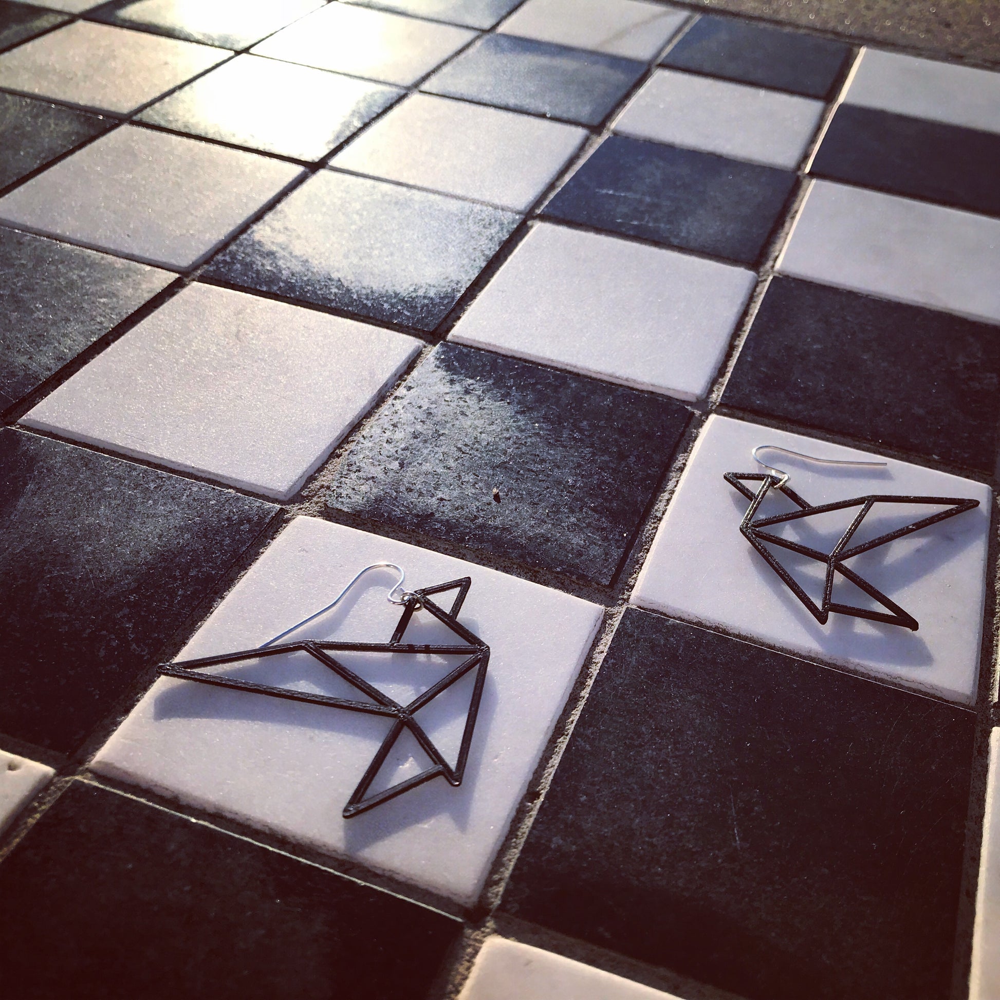Laying on a checkerboard at sunset are two geometric bird shaped earrings from R+D.