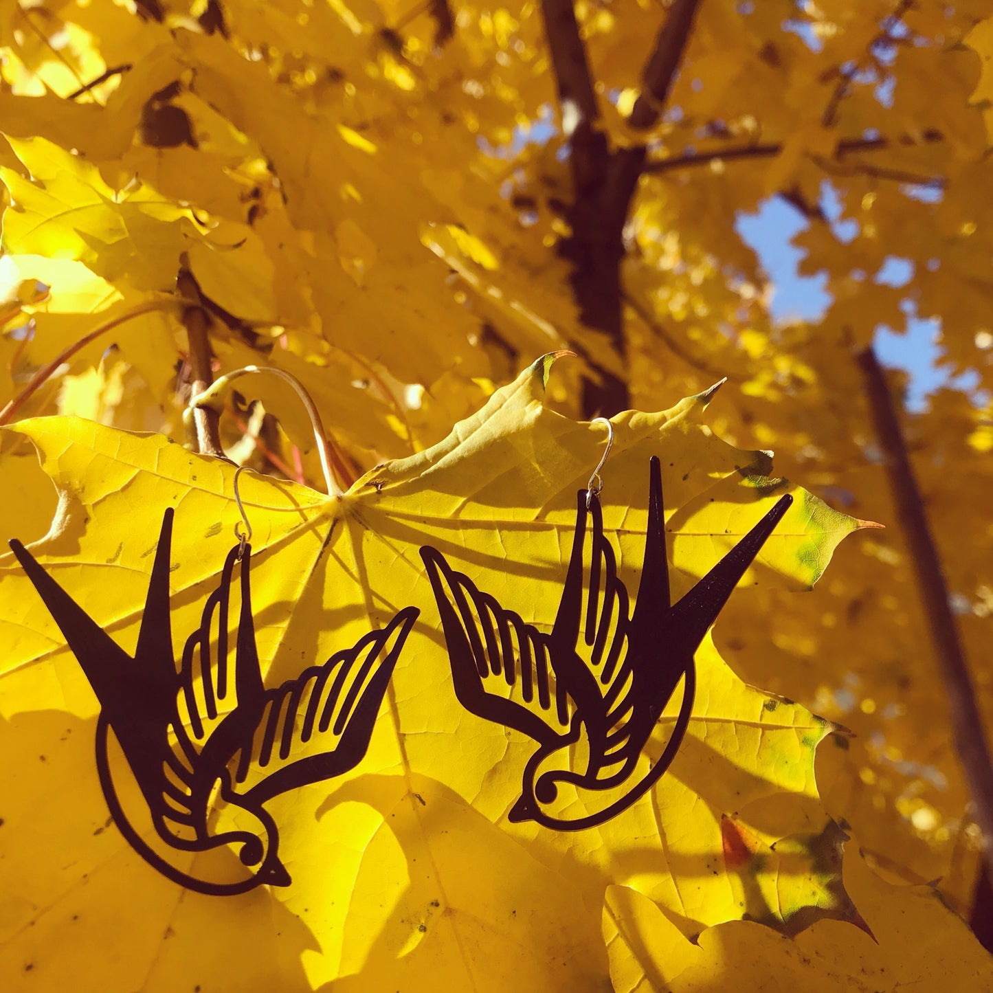 Hanging off of a bright yellow fall tree are two black R+D swallow earrings. These birds look like classic sailor tattoos, swooping down like they are flying.