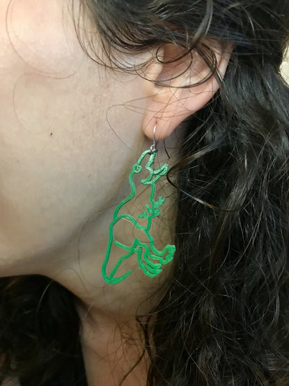 This is a close up of a woman's ear. She is wearing a 3D printed designed to look like a dinosaur. The T-Rex shape hangs from the hook as though the dinosaur were reaching to bite the earlobe. It is made with our bright kelly green plant based filament. 