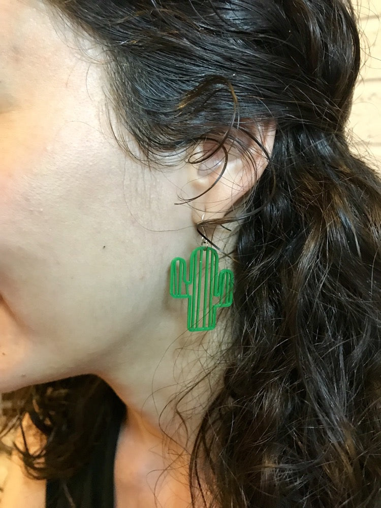 This is a close up of a woman's ear. She is wearing a bright green cactus earring. It has two arms sticking out and vertical stripes. 