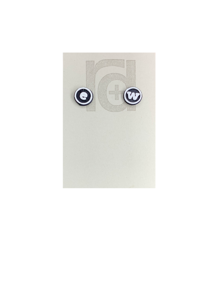 Shown on a grey r+d earring card are two 3d printed studs. They are black and white and shaped as typewrited studs. Customers can personalize these earrings to the initials they want to be printed. These have the letters e and w printed. 