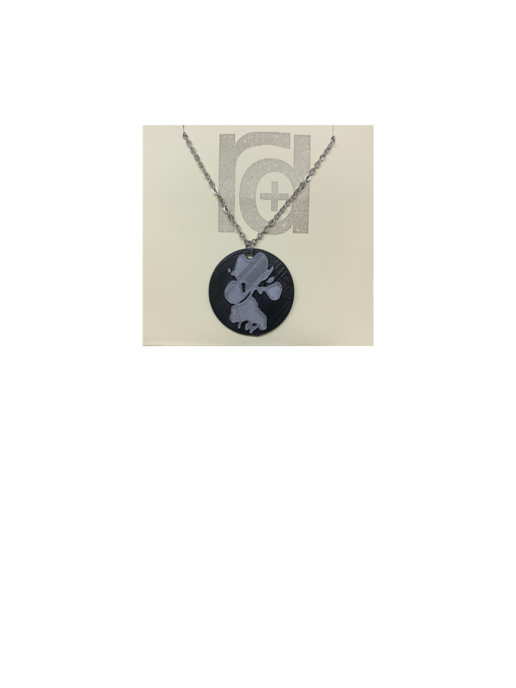 Shown on a tan recyclable necklace card is a 3D printed pendant. The pendant is a black 1 inch circle with a silver paw print. The paw print is from a large dog walking through water and the owner submitting a picture of it. 