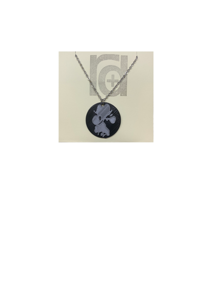 Shown on a tan recyclable necklace card is a 3D printed pendant. The pendant is a black 1 inch circle with a silver paw print. The paw print is from a large dog walking through water and the owner submitting a picture of it. 