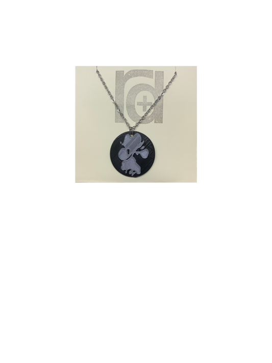 Shown on a tan recyclable necklace card is a 3D printed pendant. The pendant is a black 1 inch circle with a silver paw print. The paw print is from a large dog walking through water and the owner submitting a picture of it. 