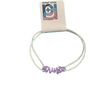 With an R+D tag, there is bracelet with a 3D printed charm. The adjustable cord on the bracelet is a white organic cotton. The charm is light purple and says trust in cursive writing.