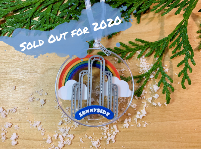 An image of our limited edition ornament for 2020--It features the art deco arch in Sunnyside, Queens, NYC, with a rainbow and clouds behind it. When you flip it over, there is a small fairy door at the borrow of the arch. 