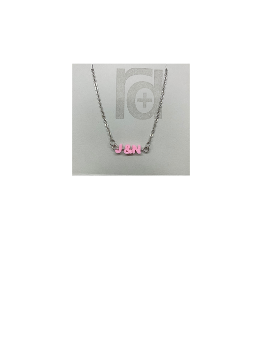 On a grey necklace card is a necklace with small letters on a metal bar. The letters are like beads and will rotate and move around. This necklace has 3 characters (J&N) in a light pink. 