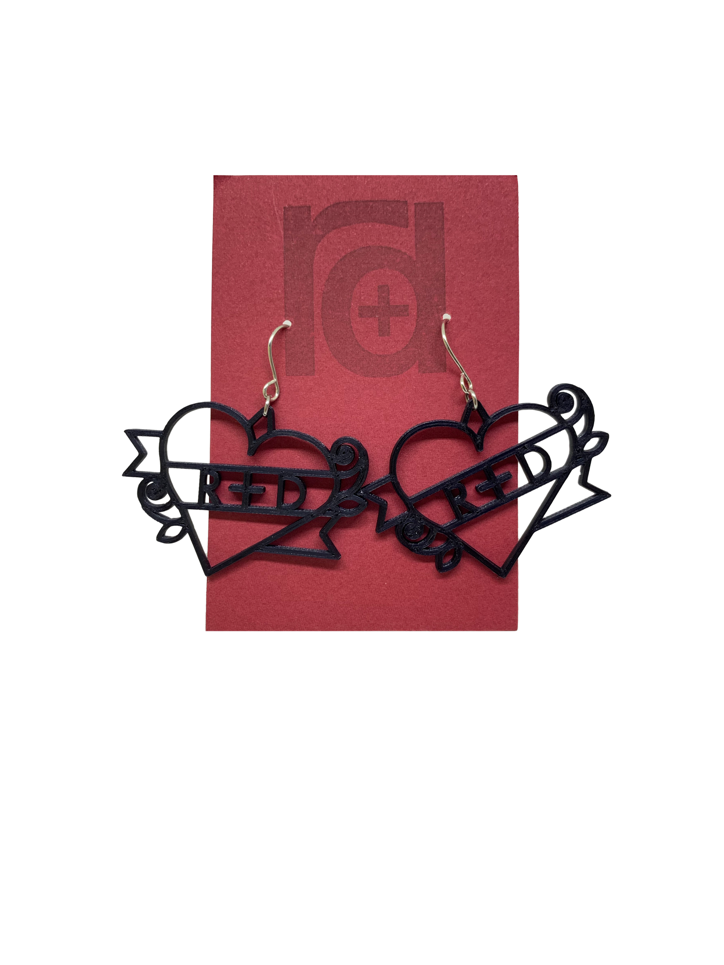 On a dark red earring card are two black R+D earrings. The earrings are shaped as hearts with a banner twisted around it and two small roses. On the banner is reads R+D, which can be personalized to say anything.