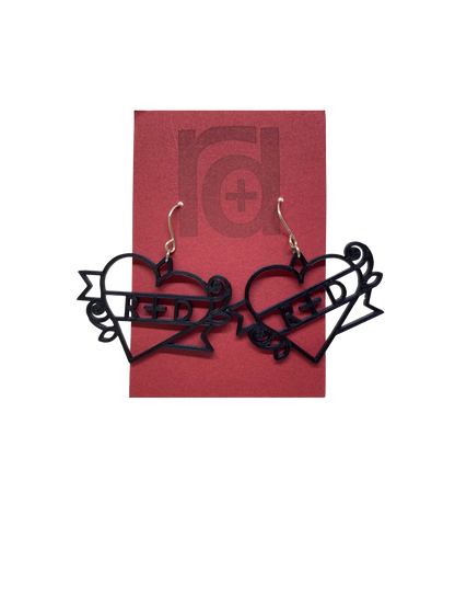 On a dark red earring card are two black R+D earrings. The earrings are shaped as hearts with a banner twisted around it and two small roses. On the banner is reads R+D, which can be personalized to say anything.